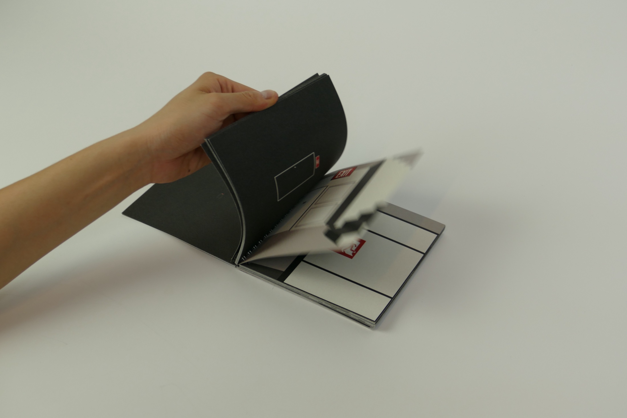A hand turning the black pages of the spiral-bound EXIT book