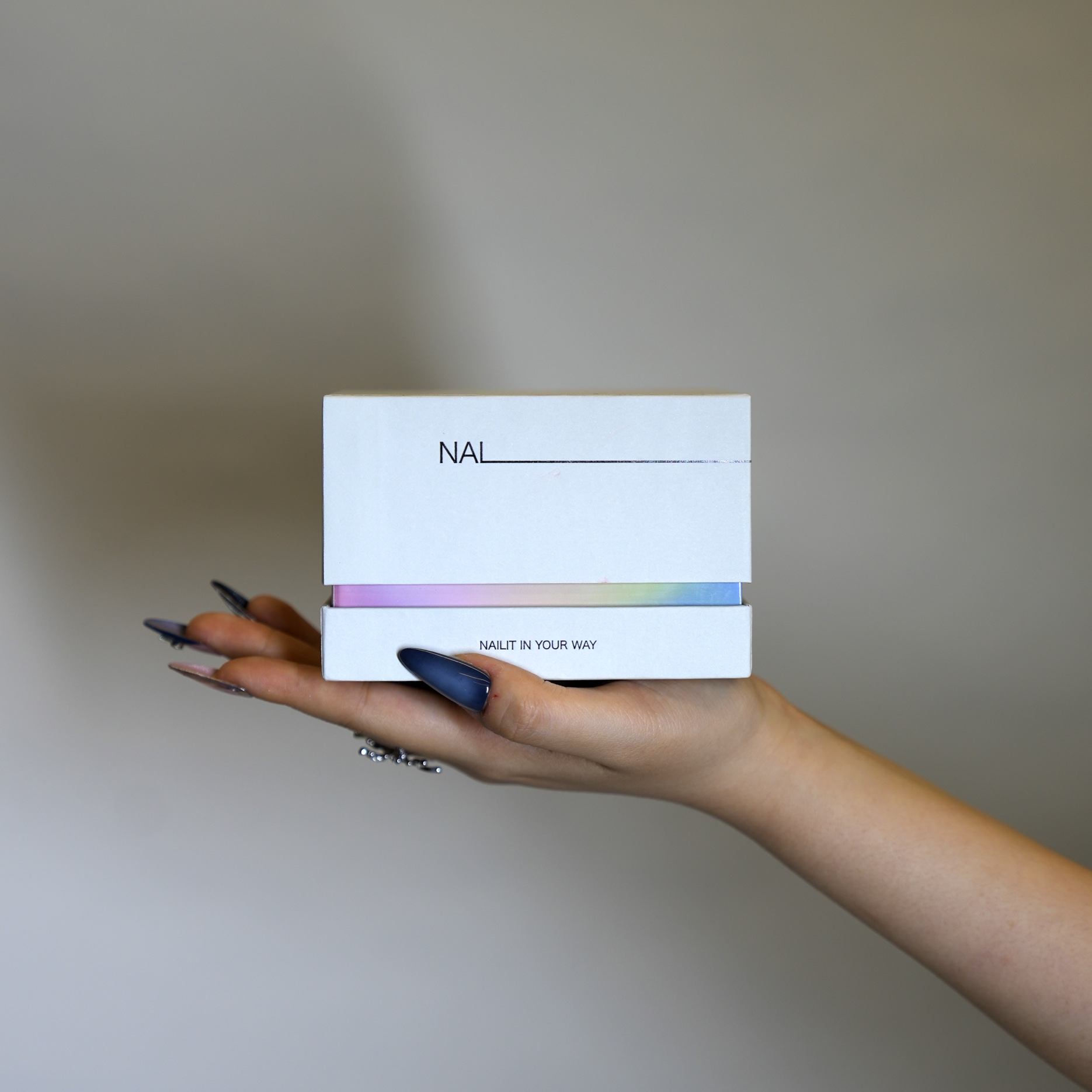 A hand holding the NAILIT primary box, opened to reveal the coloured inner layer